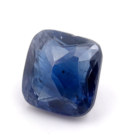 A faceted cushion-cut blue gemstone, likely a sapphire, shown on a clean white background.